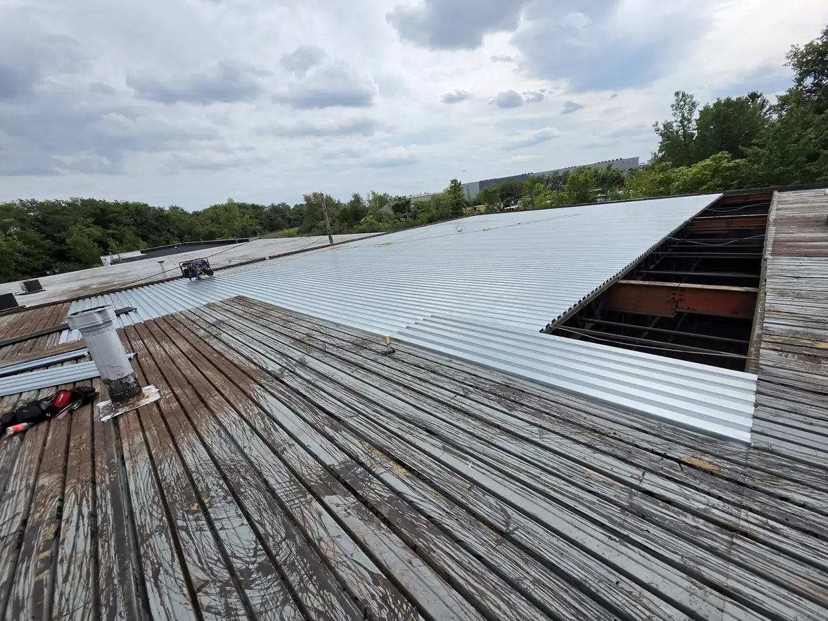 New galvanized steel roof deck panels installed next to the old weathered deck on a commercial building