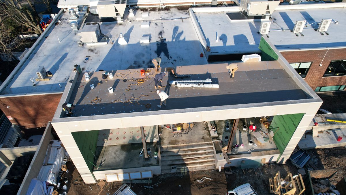 Drone view of a ProTech crew fastening cover board over insulation on a new flat roof addition to a brick commercial building
