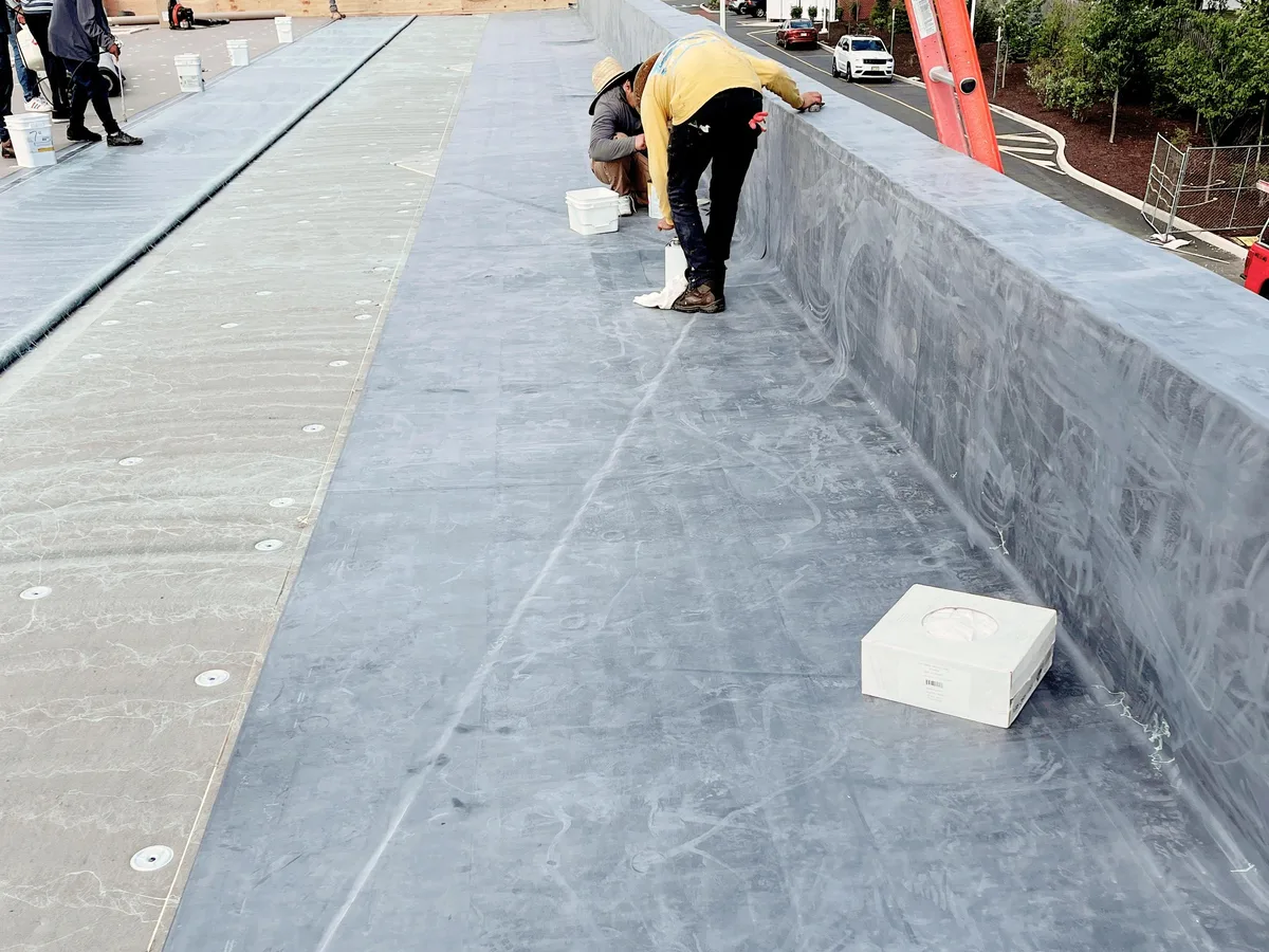 Roofers flashing a parapet wall with EPDM membrane on a new commercial building