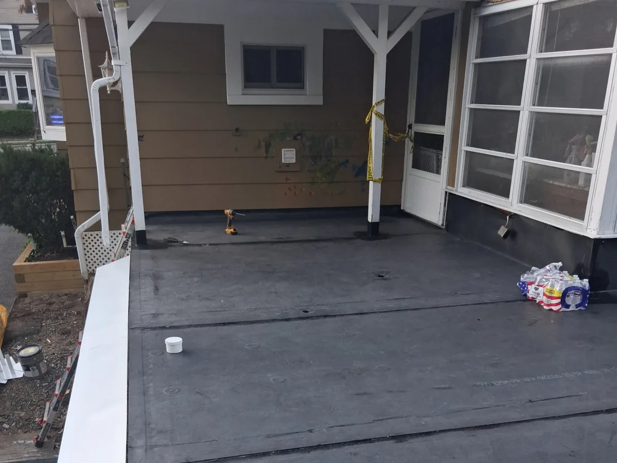 New EPDM rubber membrane on a porch roof, turned up the house wall, with new white edge metal along the outside edge