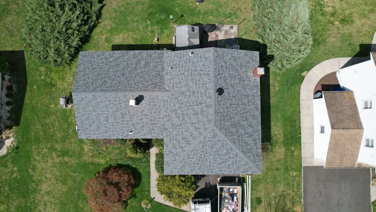 Aerial view of a hip-roof home on a large lawn with new light gray architectural shingles