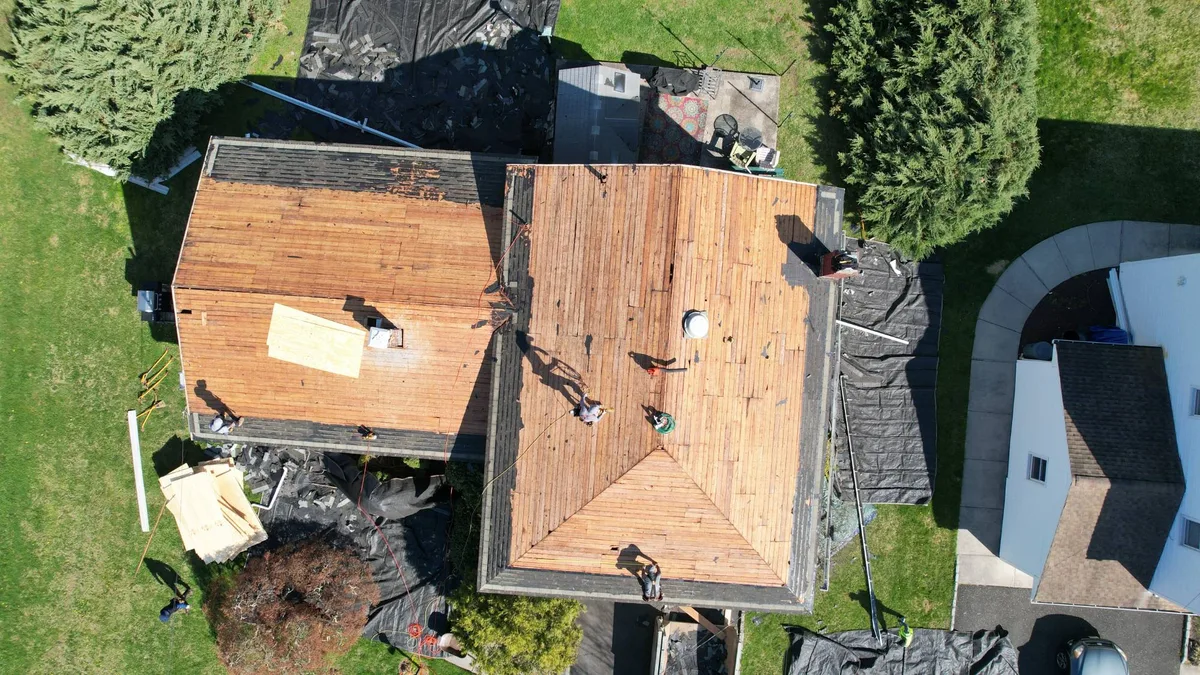 Aerial view of a hip-roof home stripped to bare decking with new plywood patches and the crew at work