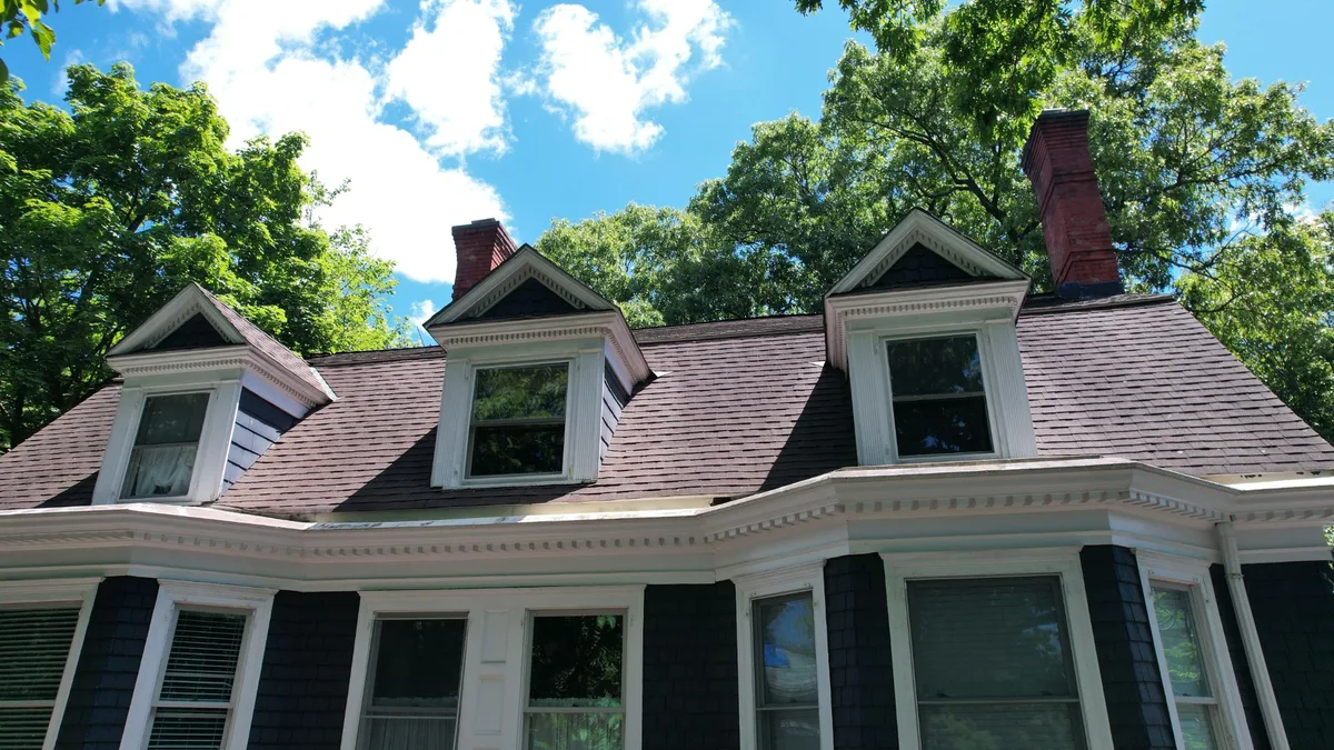 Front view of an older home with three dormers, dentil trim and two brick chimneys under a shingle roof