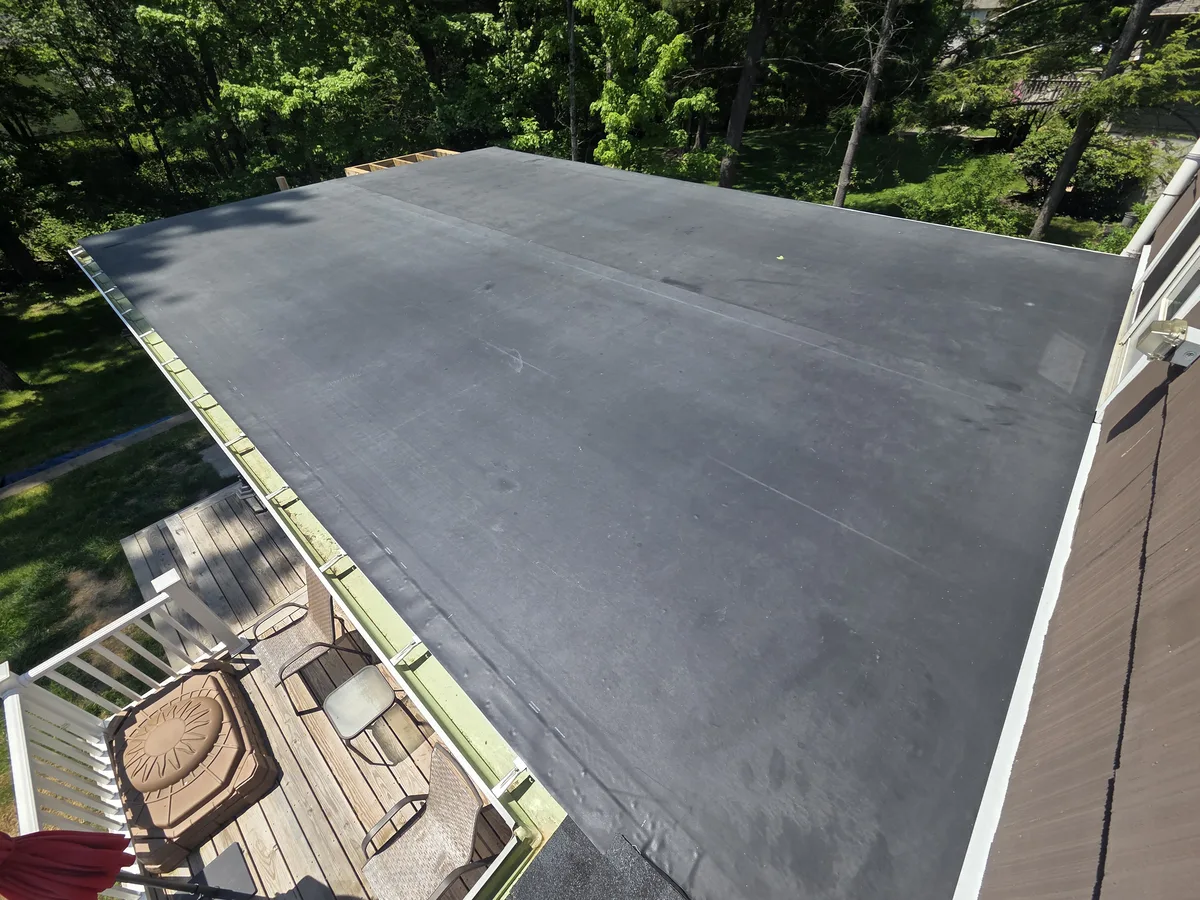 Large EPDM rubber roof over a deck and sunroom on a wooded lot, seen from above