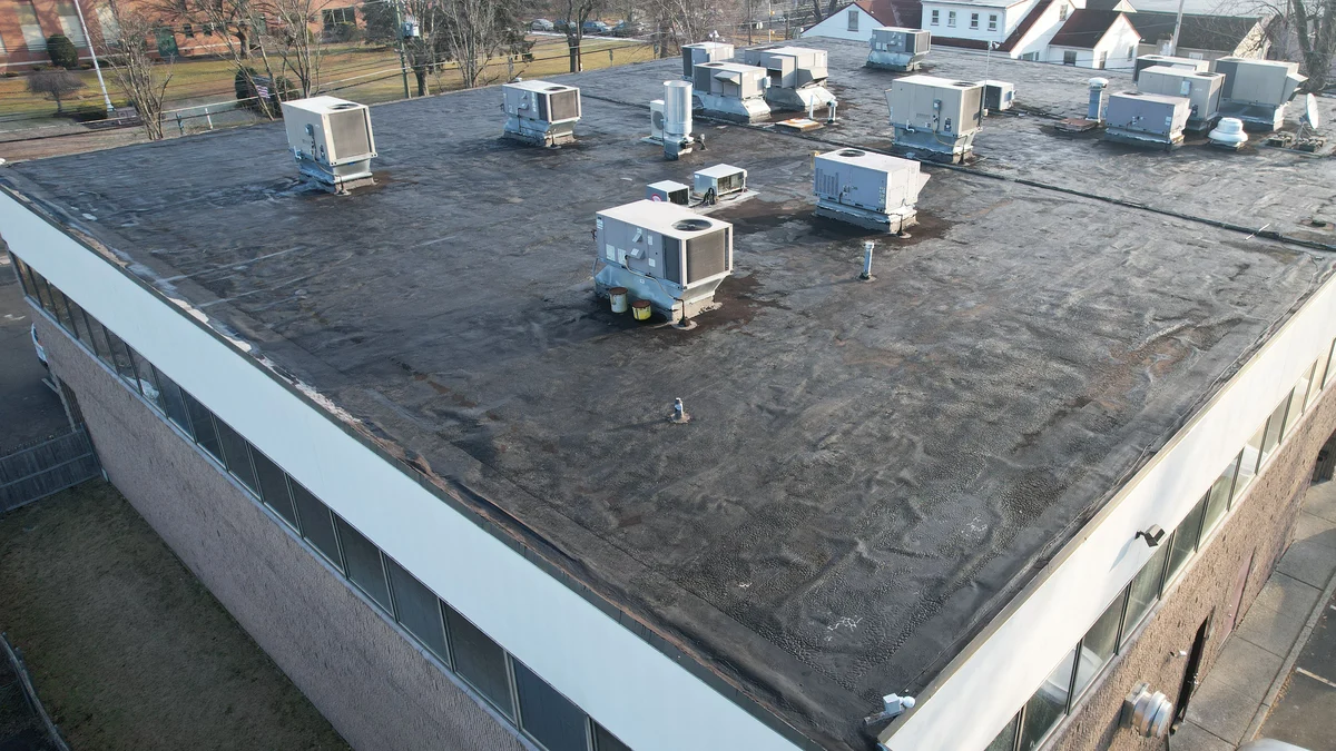 Drone photo of a two-story office and retail building in Little Falls, NJ, with a dark flat roof covered in rooftop units, seen from above at an angle
