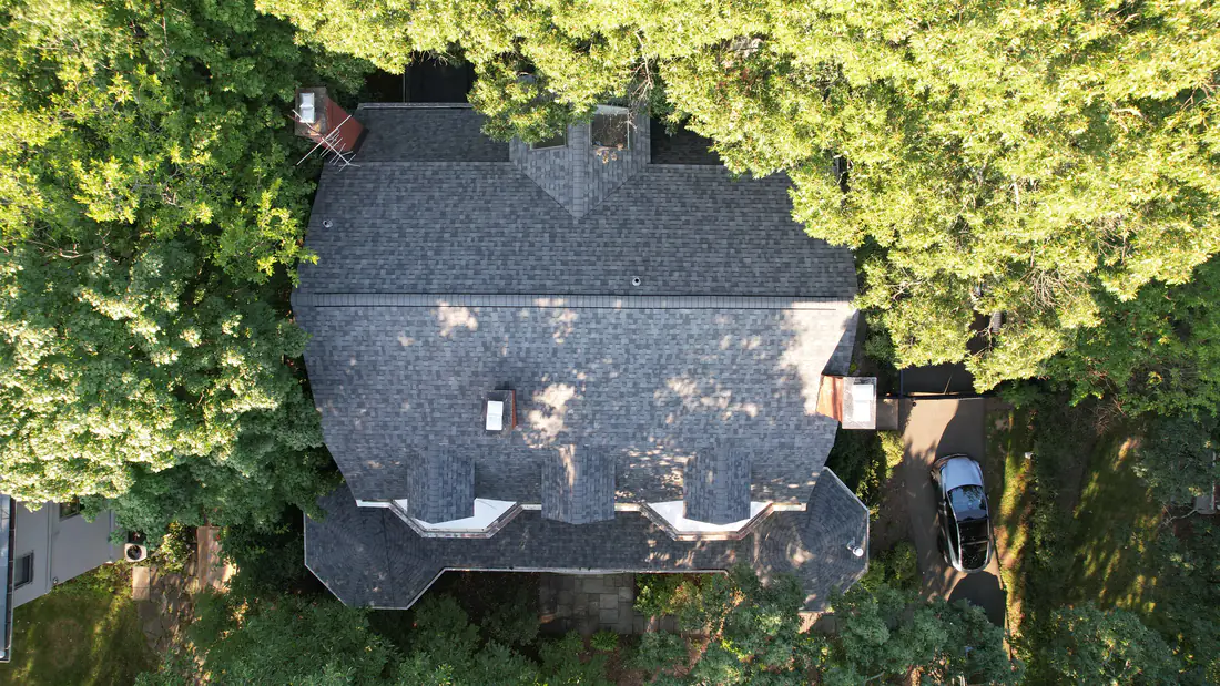 Livingston roof replacement seen from above: new Owens Corning Estate Gray architectural shingles on a large house with three front dormers, surrounded by tall trees