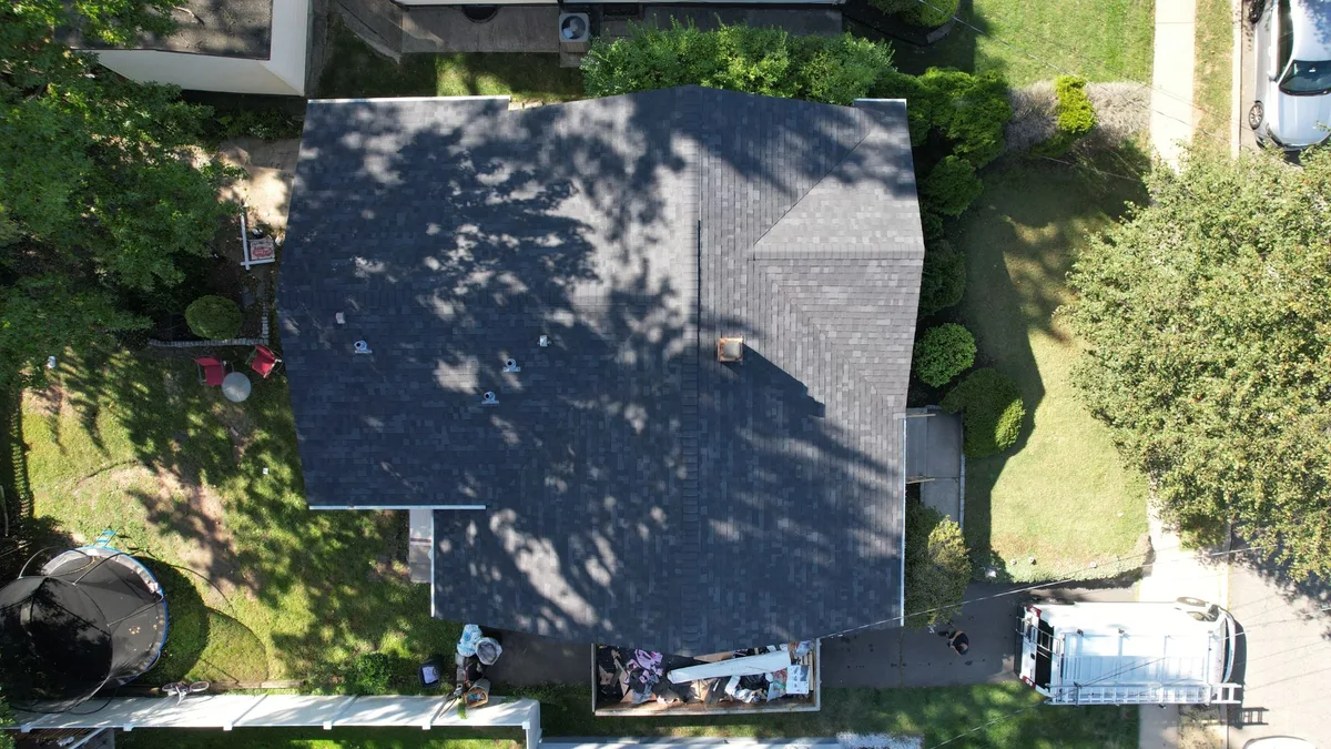 Aerial view of a new charcoal architectural shingle roof on a suburban home with mature trees