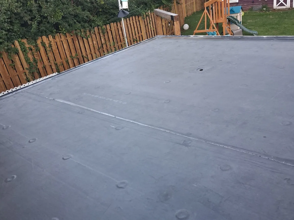 New black EPDM rubber roof on the low-slope rear roof of a home, seams taped, with a backyard fence beyond