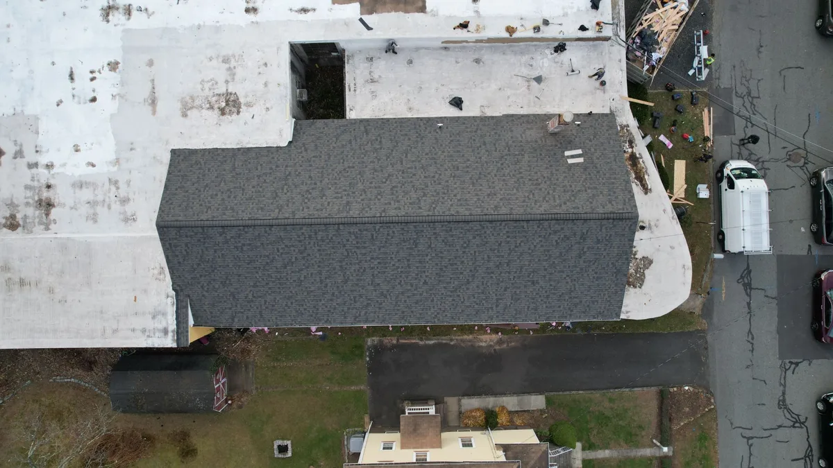 Aerial view of a new gray architectural shingle roof on a home that shares a wall with a commercial building with a white flat roof
