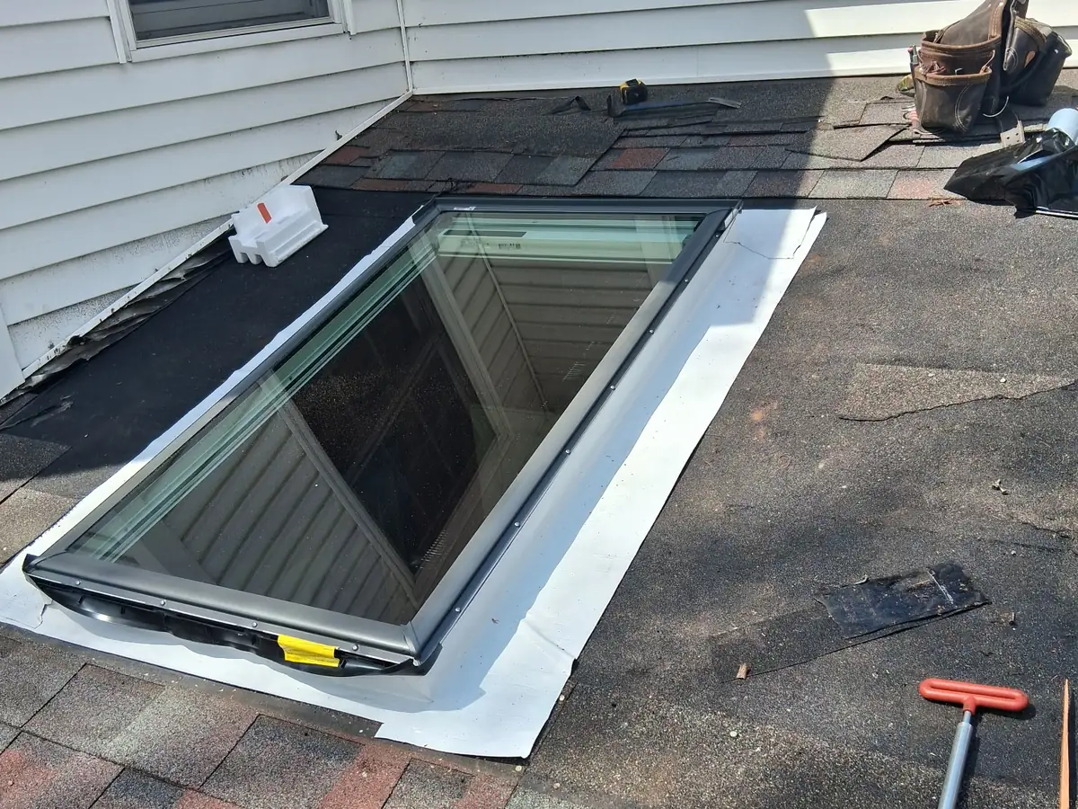 A new skylight set in the roof opening with white waterproofing membrane wrapped from the roof up onto the frame, before the flashing kit and shingles go on
