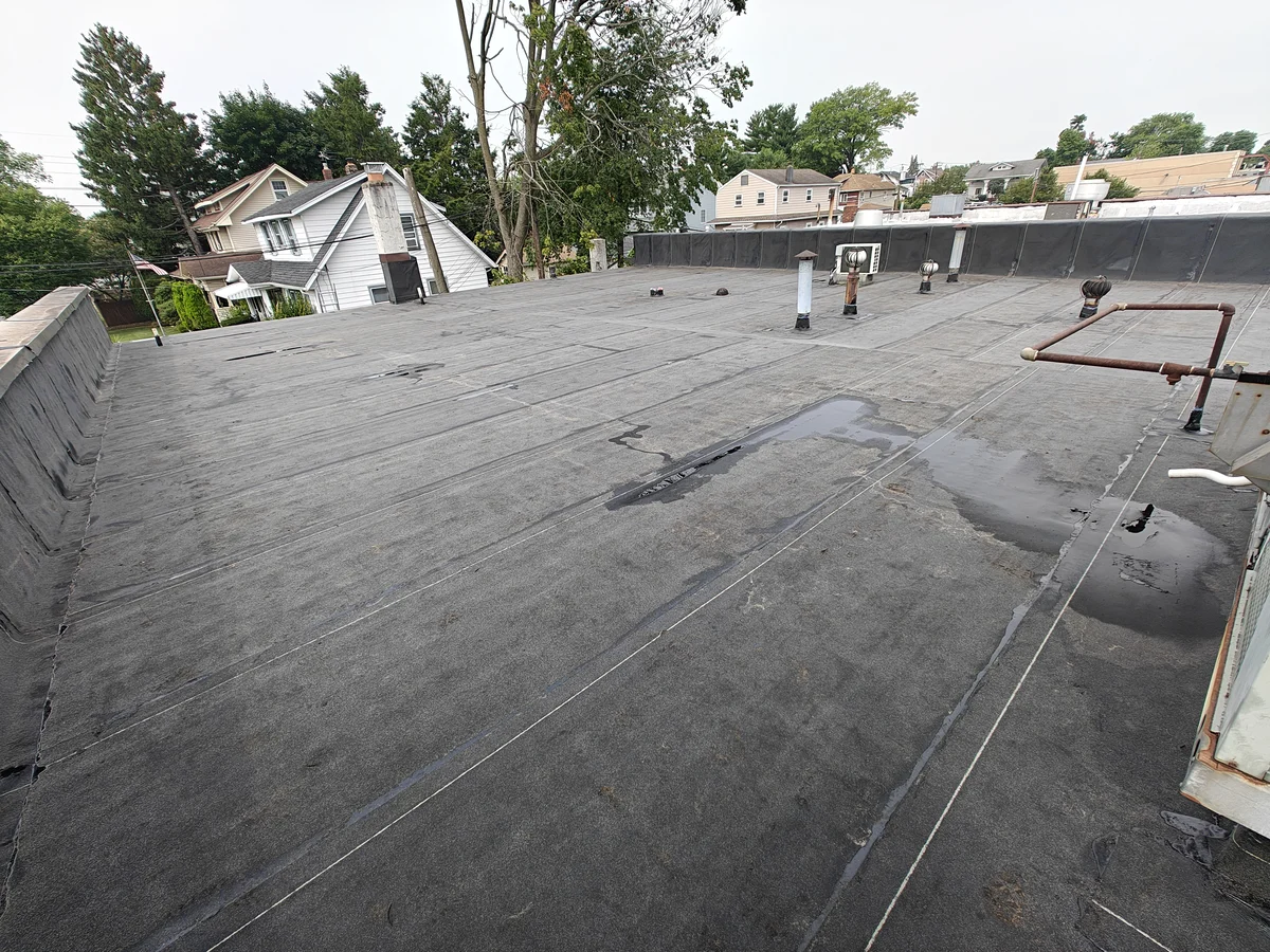 New modified bitumen roof on an office building in Oradell, NJ, looking toward the far parapet wall wrapped in the same membrane, with turbine vents and vent pipes flashed in