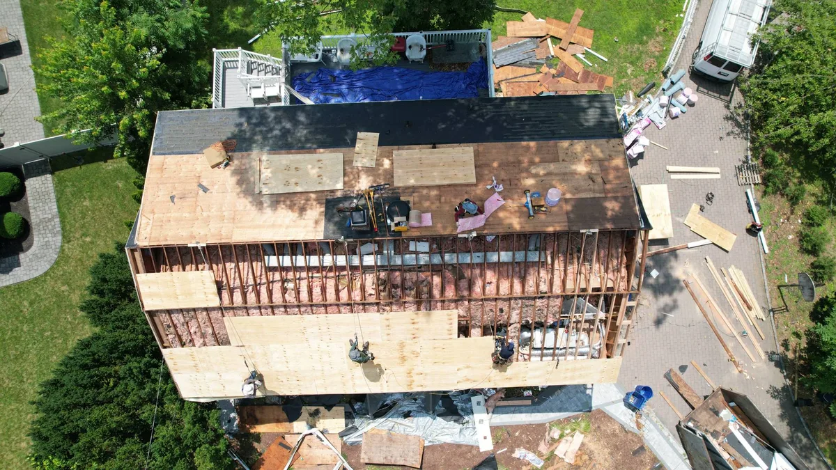 Aerial view of a large home with new plywood roof decking being installed over the rafters