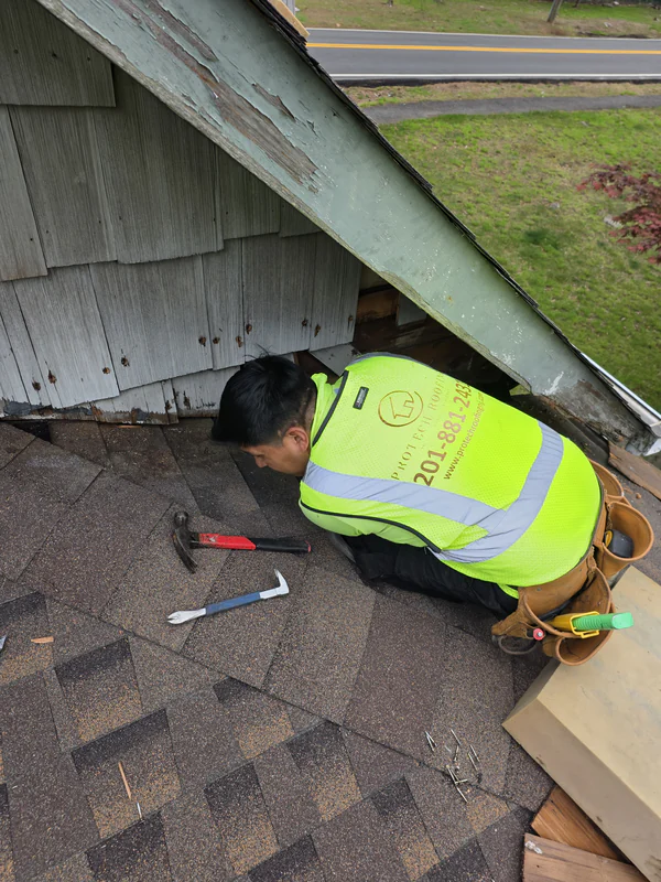 ProTech roofer in a company vest working on worn wood at the base of a gable wall, where it meets the roof