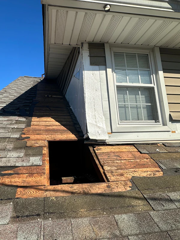 Damaged roof decking cut out next to a dormer, leaving an opening to the attic