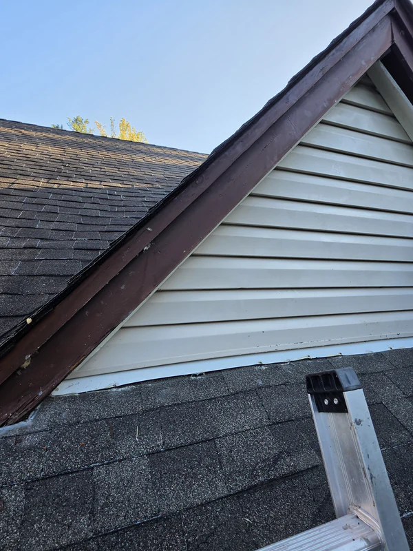 Before the repair in Mahwah: weathered brown rake trim boards on a gable above a lower shingle roof, with an open gap where the bottom of the siding meets the shingles