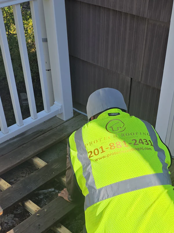 ProTech roofer in a company vest with the deck boards pulled up to reach the roof underneath a balcony deck