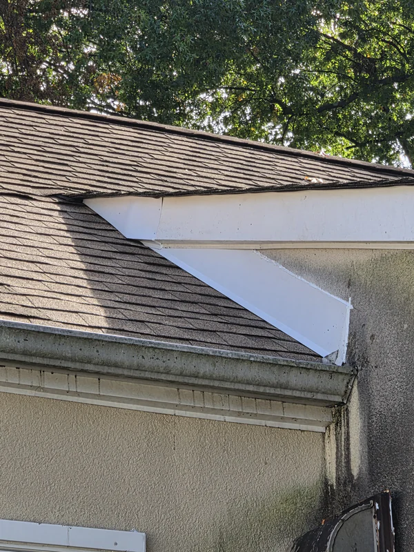 After the repair in Upper Saddle River: new white metal counter-flashing where a shingle roof meets a stucco wall, and custom flashing where the lower and upper roofs meet at the wall