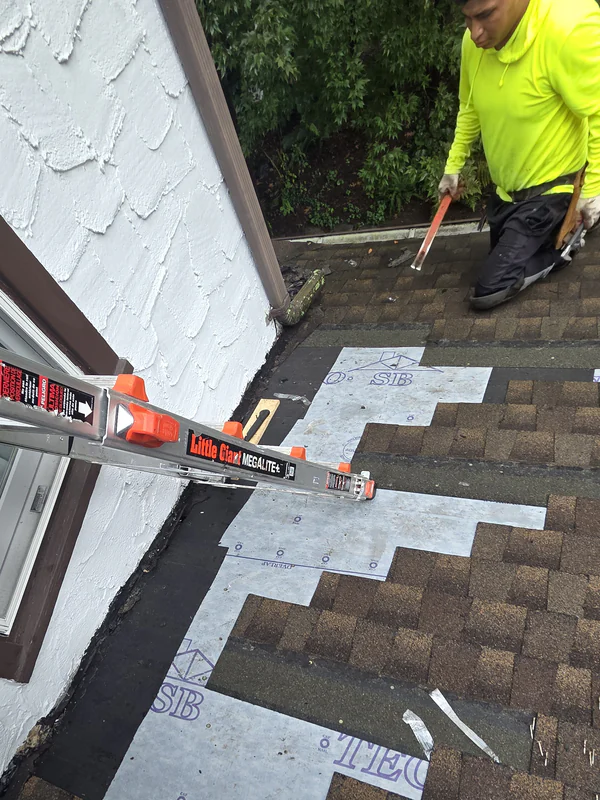 Shingles removed along a stucco wall, with new underlayment laid along the wall and a ProTech roofer at work