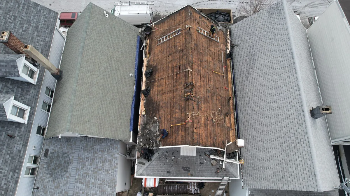 Aerial view of a rowhouse roof stripped to bare decking in winter with the crew at work