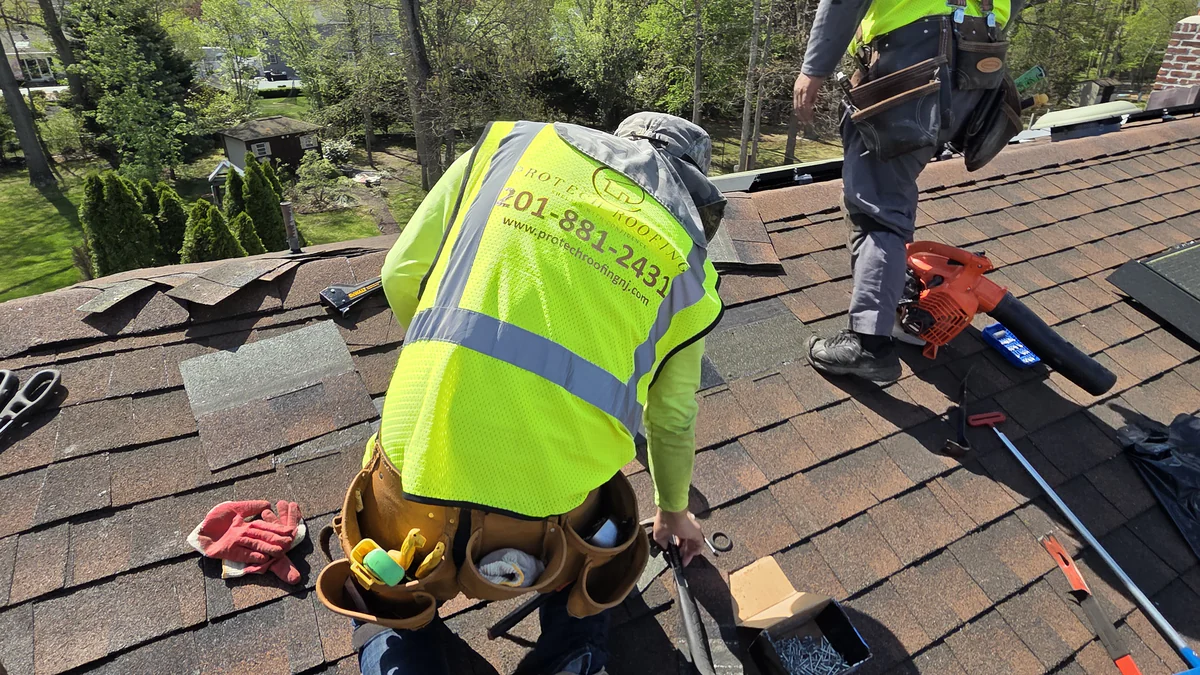Two ProTech roofers in company safety vests repairing a shingle roof