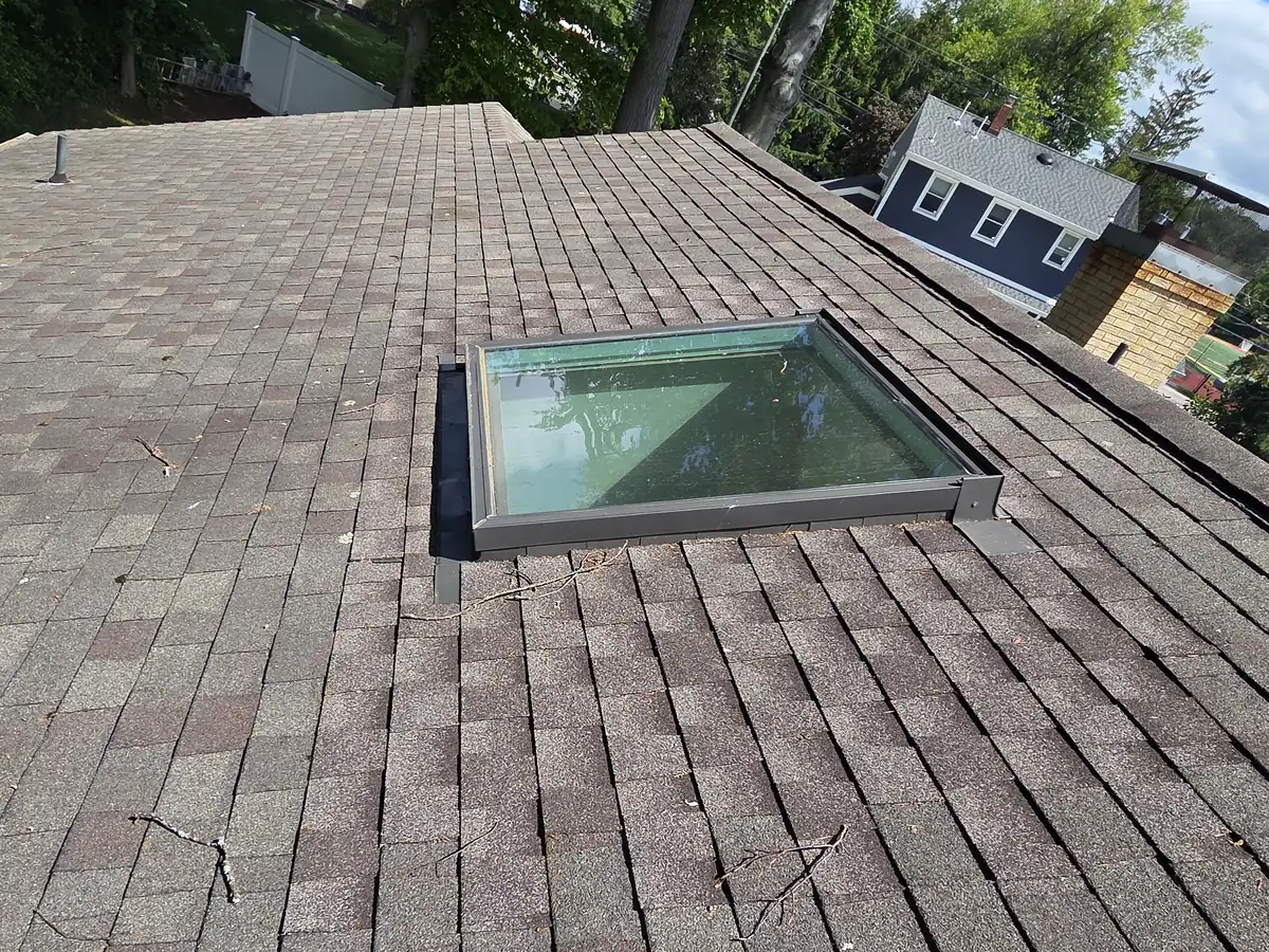 A skylight with metal flashing in an older, weathered shingle roof