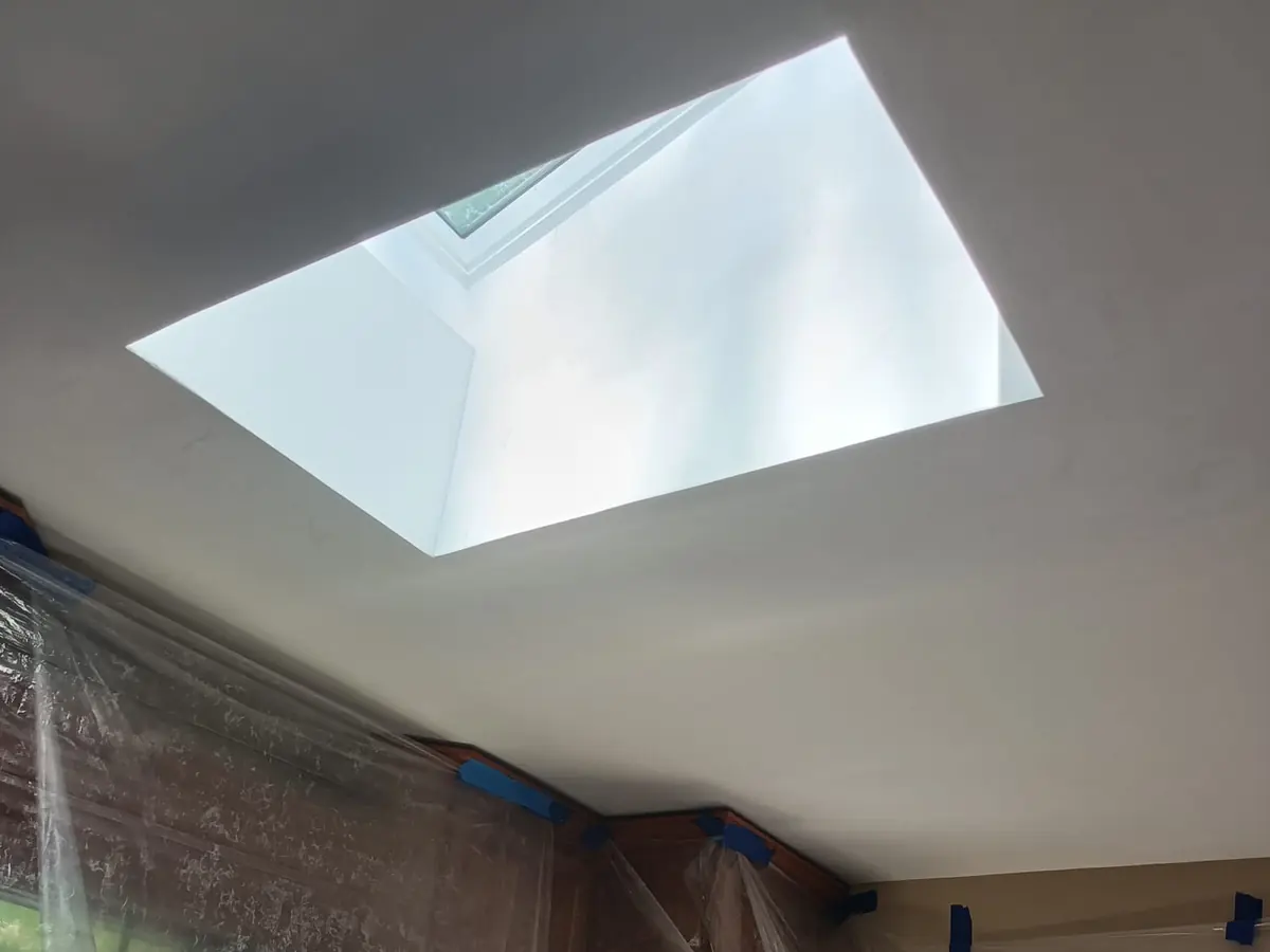 View from inside a room up a painted skylight light shaft, with the walls covered in plastic sheeting during the work