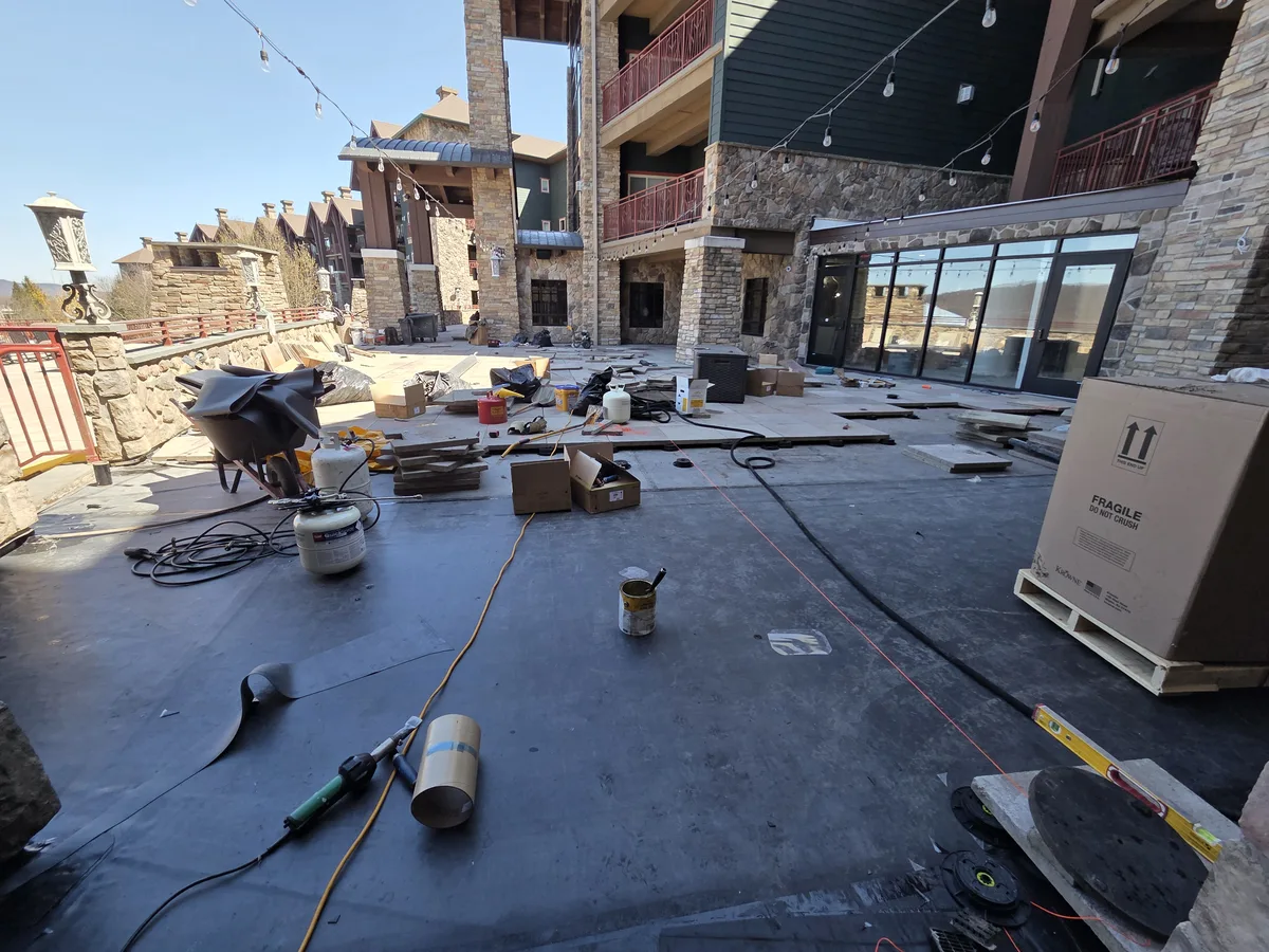 Black EPDM waterproofing membrane on a terrace deck at a stone-clad building, with paver pedestals and pavers being set