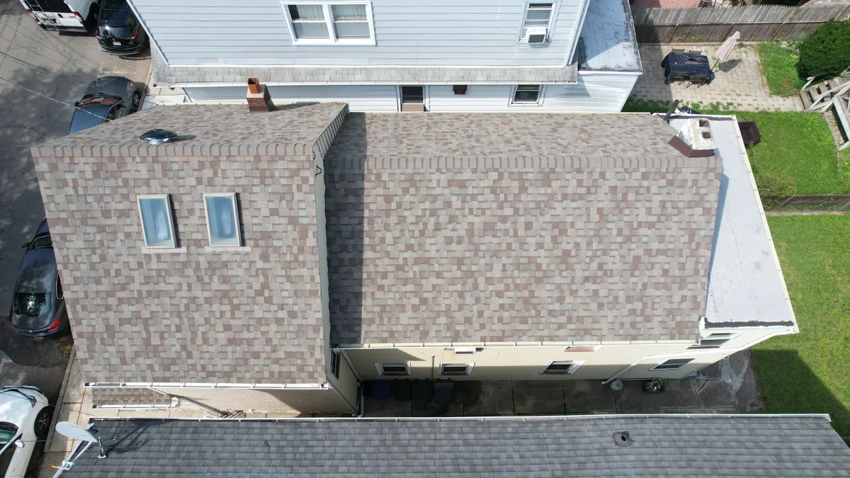 Aerial view of a new tan-blend architectural shingle roof with two new skylights on a two-family home