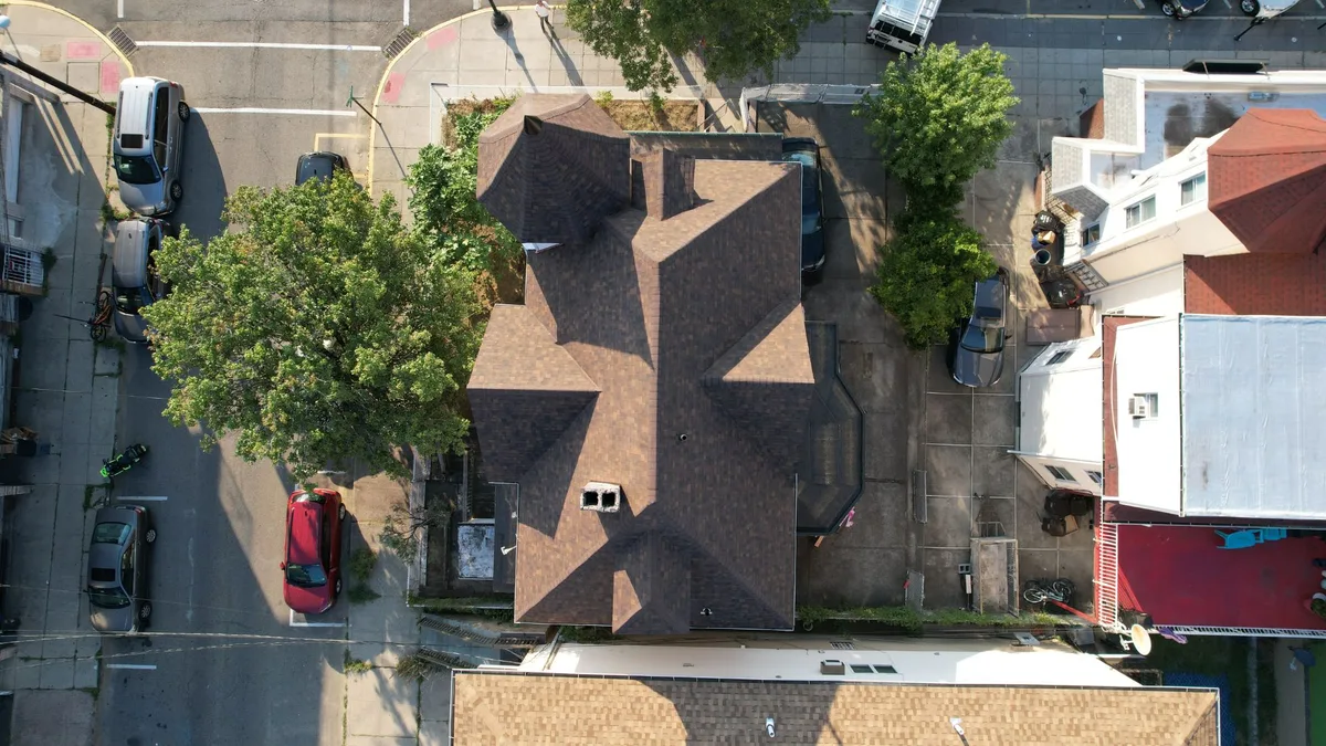 Aerial view of a Victorian home with a turret after a full roof replacement with dark brown architectural shingles